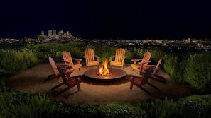 A circular seating arrangement with a central fire feature, surrounded by greenery and overlooking a cityscape at night. - PUBLIC West Hollywood (West Hollywood)