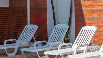 Zona junto a la piscina con sillas reclinables blancas y un aplique negro fijado a la pared.