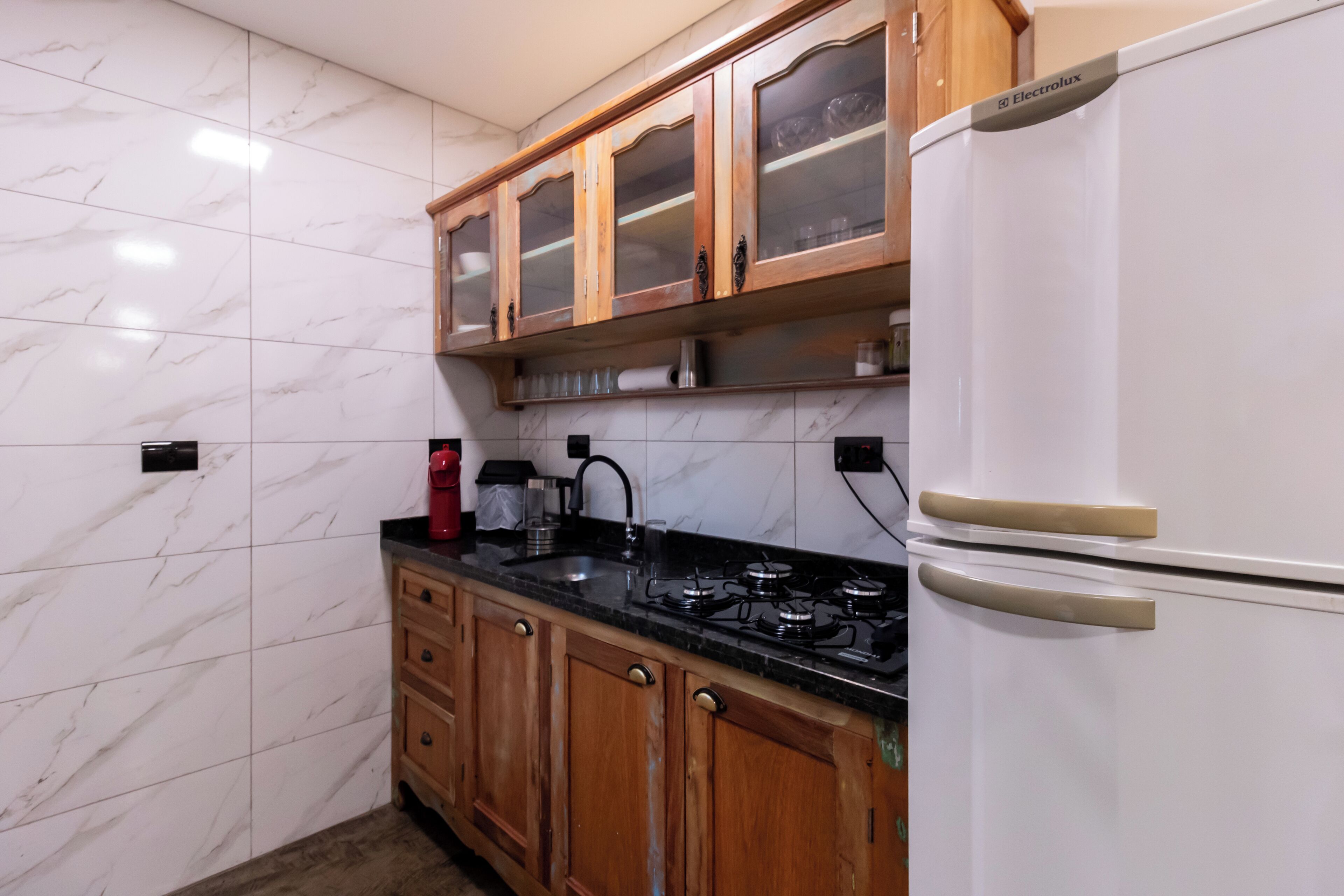 Una cocina con baldosas de mármol, armarios de madera, una estufa a gas y un refrigerador blanco.