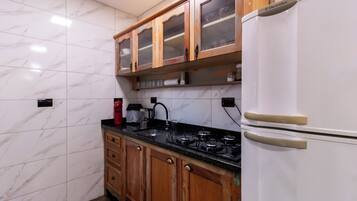 Una cocina con baldosas de mármol, armarios de madera, una estufa a gas y un refrigerador blanco.