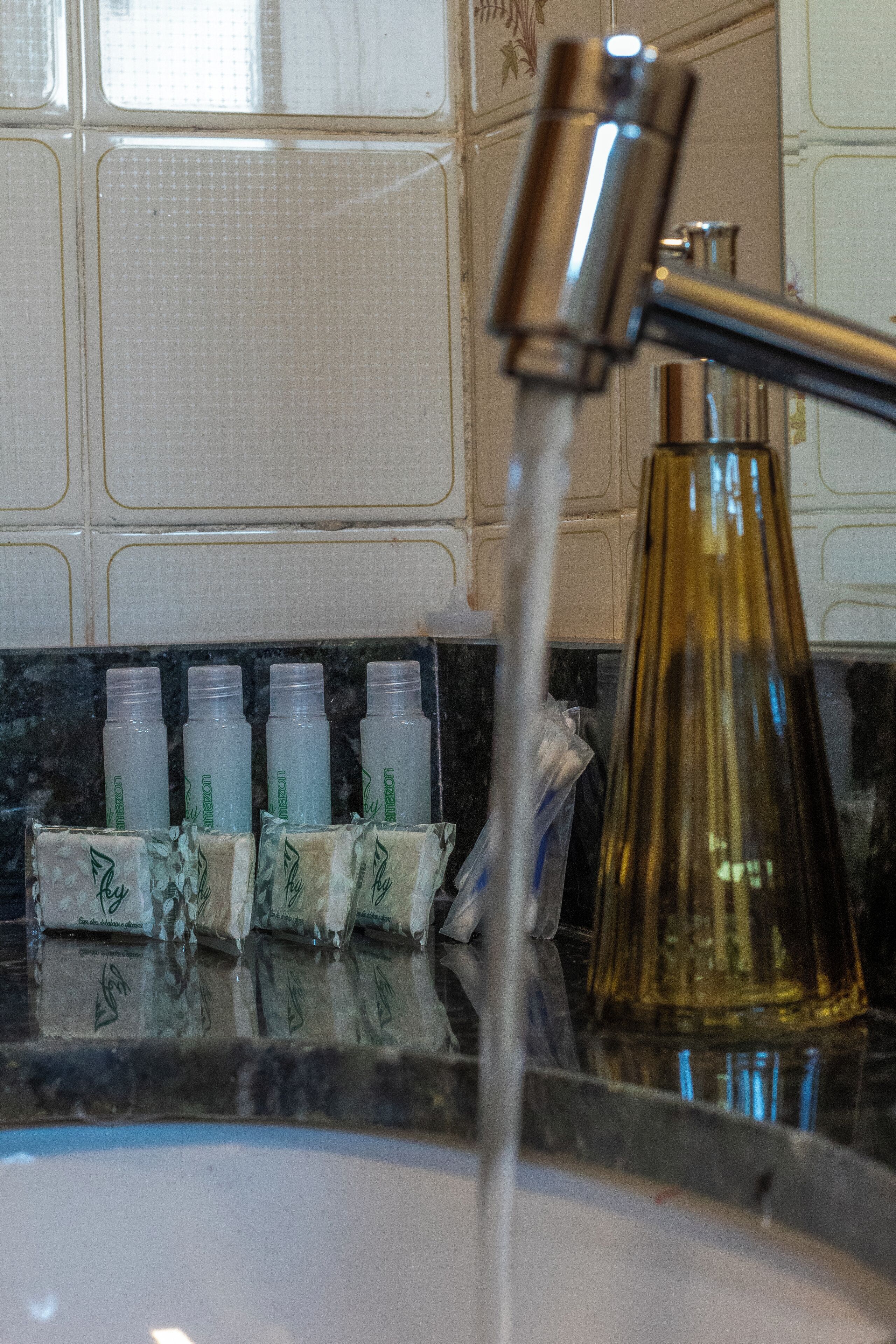 Un lavabo avec de l’eau courante, un flacon de savon liquide et une bouteille en verre.