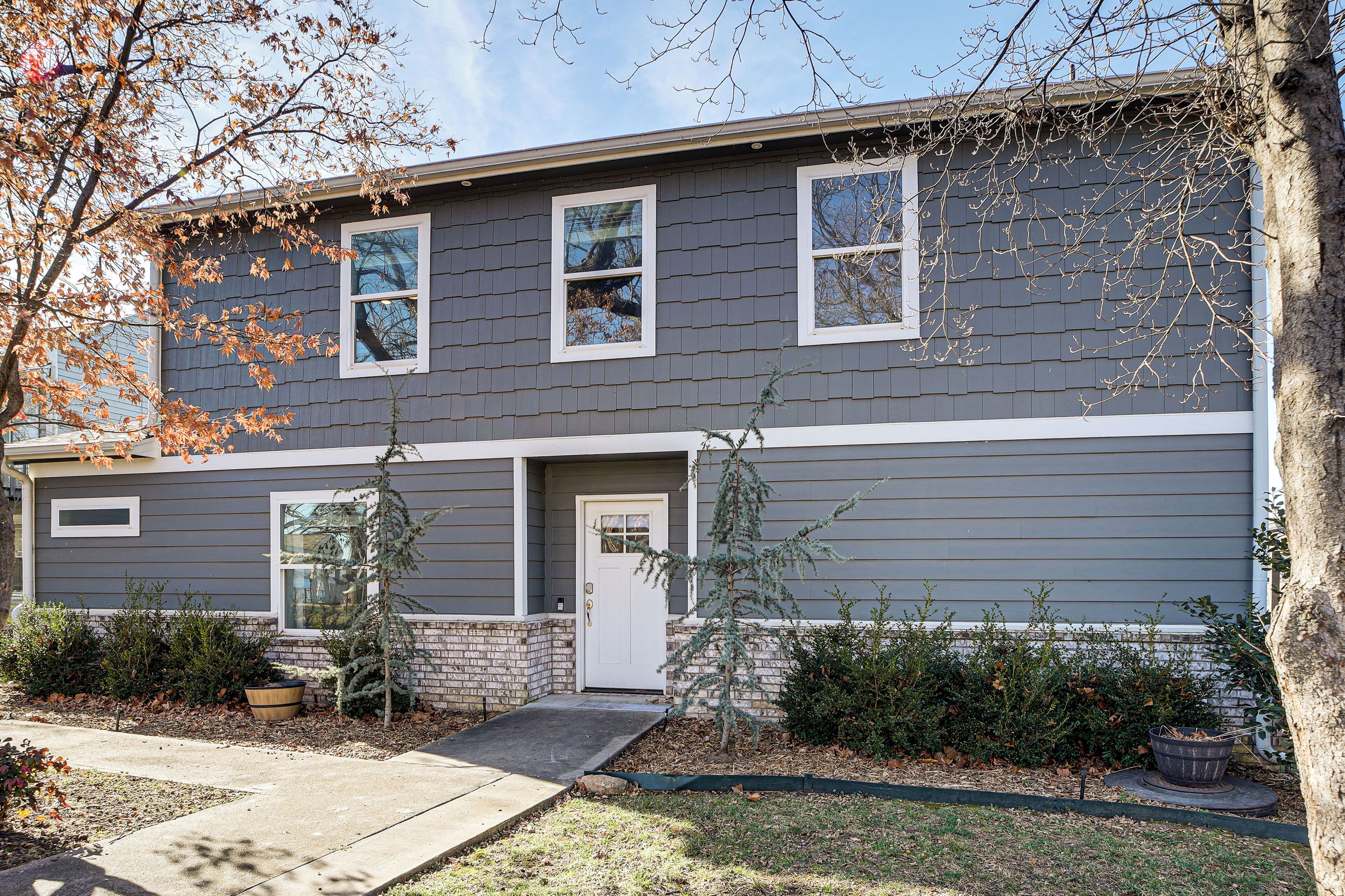 A two-story residential building with a gray exterior, white trim, and a front door with a small porch.