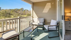 A balcony with a view of a forest, a chair, a table, and a lamp. - Pool & Hot Tub Access: True Blue Golf Resort Condo (Pawleys Island)