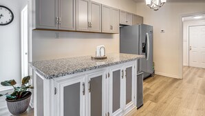 A kitchen with grey cabinets, a granite countertop, a stainless steel refrigerator, and a potted plant.