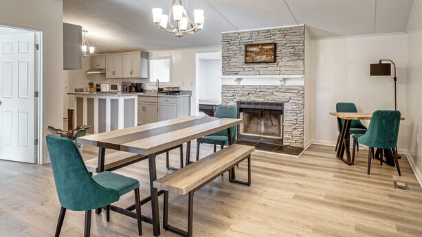 A spacious kitchen with a stone fireplace, a dining area with a long table and chairs, and a modern chandelier.