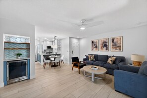 A modern living room with a blue sofa, a coffee table, and a dining area with a white table and chairs. - Waterfront 2-bed 2-bed Just a Short Walk from Beach (Madeira Beach)