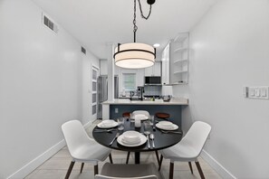 A modern kitchen with white cabinetry, a central island, and a dining area with a round table and white chairs. - Waterfront 2-bed 2-bed Just a Short Walk from Beach (Madeira Beach)
