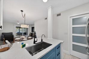A modern kitchen with a central island, a built-in sink, and a dining area with a table and chairs. - Waterfront 2-bed 2-bed Just a Short Walk from Beach (Madeira Beach)