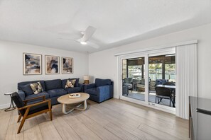 A modern living room with a blue sofa, a wooden coffee table, and a ceiling fan. - Waterfront 2-bed 2-bed Just a Short Walk from Beach (Madeira Beach)