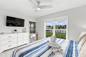 Une chambre à coucher comprenant un lit, un bureau, une chaise, un téléviseur et une fenêtre donnant sur une marina.
