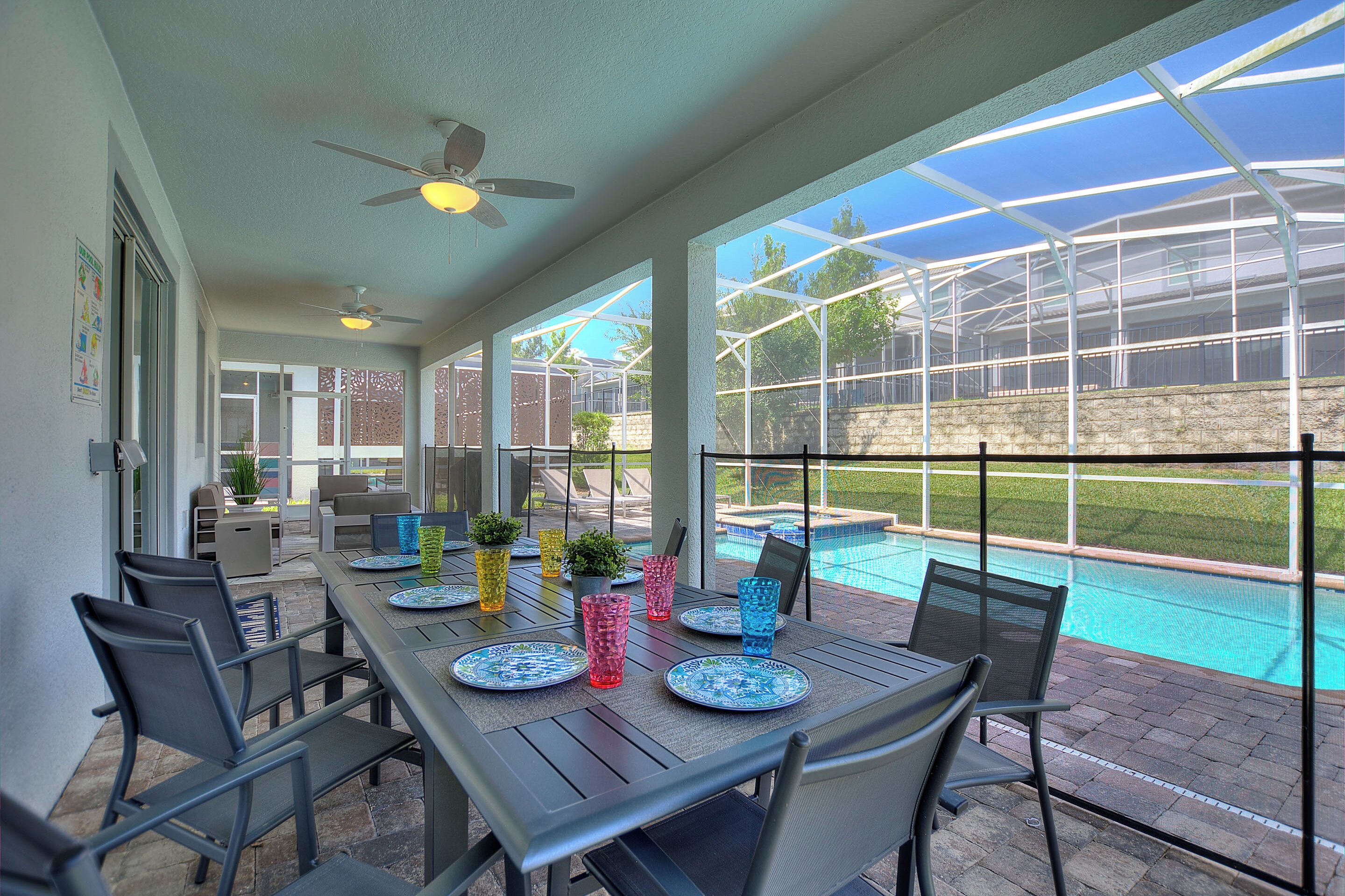 An outdoor patio with a table set for dining, a pool, and a greenhouse structure in the background.