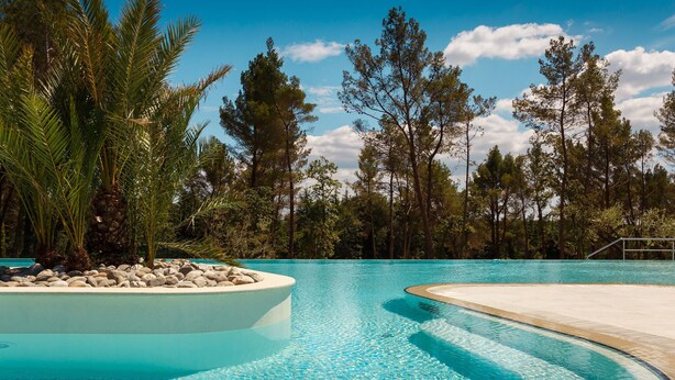 Una piscina azul cristalina rodeada de árboles y una terraza de madera.