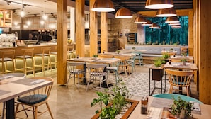 Un restaurante con vigas de madera, varias mesas y sillas, lámparas colgantes de cobre y vistas a árboles a través de un ventanal.