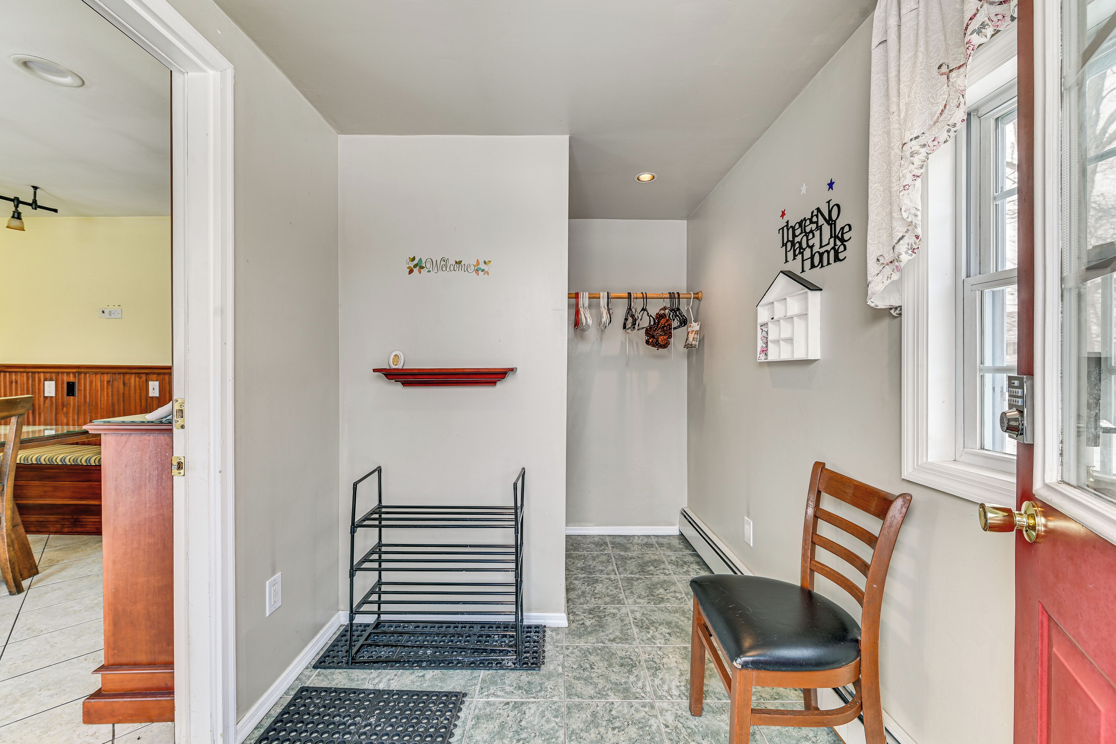 A hallway with a wooden chair, a black metal rack, a red shelf, and a welcome sign.