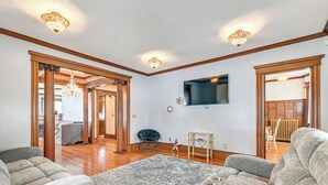Ein geräumiges Wohnzimmer mit einem großen, grauen Ecksofa, einem gemusterten Teppich und einem an der Wand montierten Flachbildfernseher.