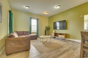 Uma sala de estar com um sofá de couro marrom, uma mesa de centro redonda, uma TV de tela plana na parede e um armário de madeira.