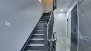 A staircase with a handrail, a door with a handle, and a light switch on the wall. - Easy NYC Access: Updated Apt Near Parks & Bay! (Mt Vernon)