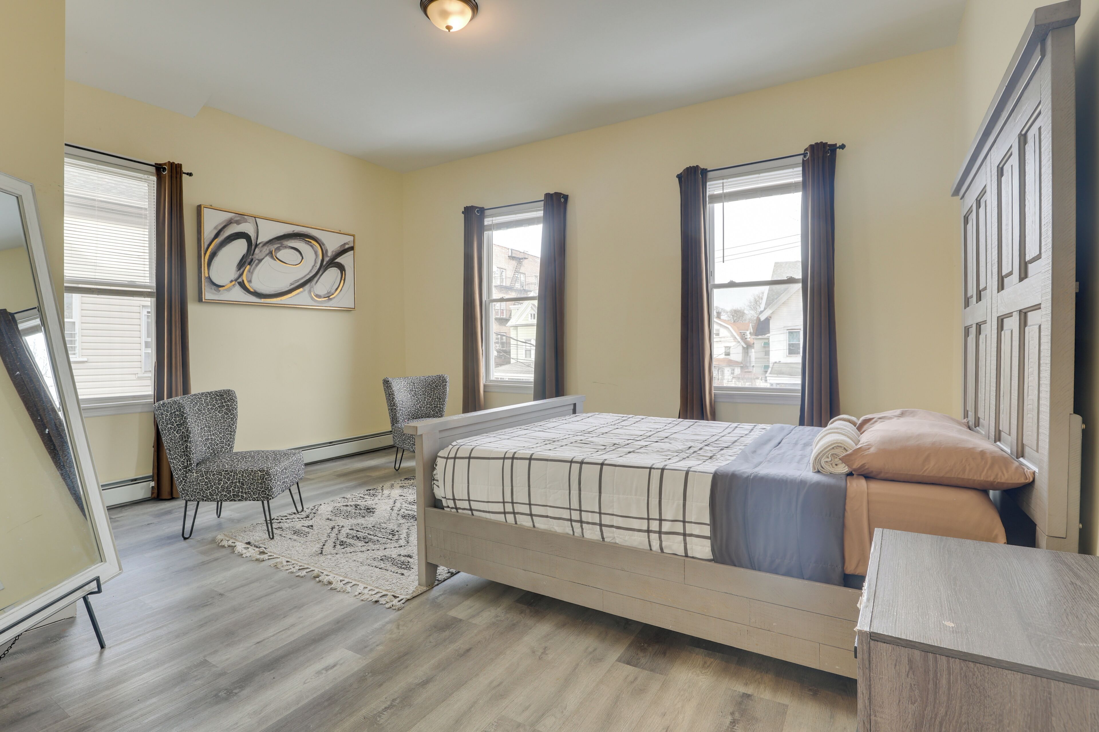 A bedroom with a bed, two chairs, a dresser, a rug, and a painting on the wall.