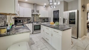 A modern kitchen with white cabinets, a stainless steel refrigerator, and a unique chandelier. - 3 Mi to Randolph AFB: San Antonio Area Home (Universal City)