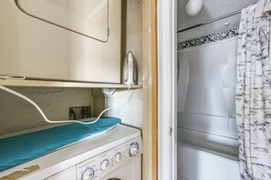 A compact laundry area with a washing machine, a drying rack, and a shower curtain. - 3 Mi to Houston Medical Center: Extended Stay (Houston)