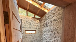 A small, rustic bathroom with a stone wall, a wooden door, and a skylight.