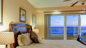 Ein Hotelzimmer mit einem großen Bett, einem Deckenventilator, Meerblick und einem Balkon mit Glastür.