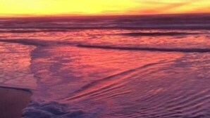 Una playa al atardecer con olas lamiendo suavemente la orilla.