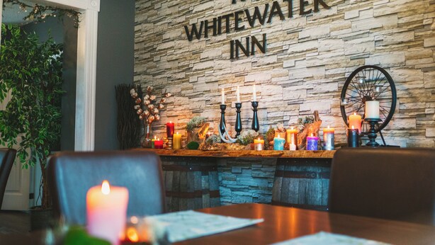 A dining area with a stone wall, candles, and a sign reading "The Whitewater Inn". - Modern, Spacious 4-Bedroom Home with Garden & Garage (Beachburg)
