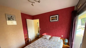 Een slaapkamer met een bed, een stoel, een bureau, een spiegel en een raam met gordijnen.