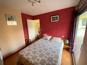 Ein Schlafzimmer mit Bett, Stuhl, Schreibtisch, Spiegel und einem Fenster mit Vorhängen.