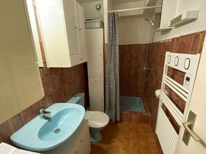 Ein kleines Badezimmer mit blauem Waschbecken, weißer Toilette und Duschbereich.