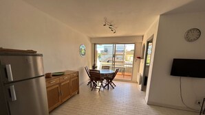 A compact kitchen with a refrigerator, wooden cabinets, a dining table with chairs, and a TV mounted on the wall. - Apartment for 4 with parking near beach (Argelès-sur-Mer)