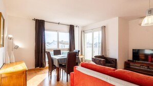 A modern living room with a red sofa, a dining table with chairs, and a TV on a wooden stand. - Bright Apartment with Terrace and Parking in Santa Margarita (Roses)