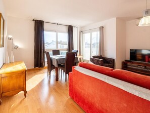 Ein modernes Wohnzimmer mit einem roten Sofa, einem Esstisch mit Stühlen und einem Fernseher auf einem Holzboden.