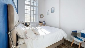 Una camera da letto con un letto, una scrivania, una sedia, una lampada, una finestra e una parete decorata con quadri.