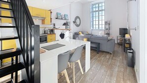 Una cucina moderna con isola centrale, un'area pranzo con sedie, un divano grigio e una scala.
