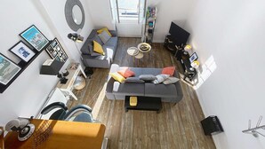 Un soggiorno moderno con un divano, un tavolino da caffè e una TV. Si vede una finestra con vista su barche e uno specchio a forma circolare appeso al muro.