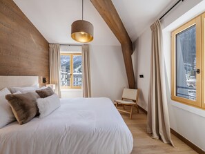 A bedroom with a large bed, a wooden ceiling, a window with a view, and a chair. - Beautiful apartment for 8 in Chamonix, central, parking, wifi (Chamonix-Mont-Blanc)