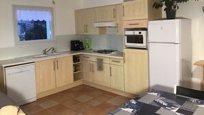 Eine kleine Küche mit hellen Holzschränken, einem weißen Kühlschrank, einem eingebauten Backofen und einem Gasherd.