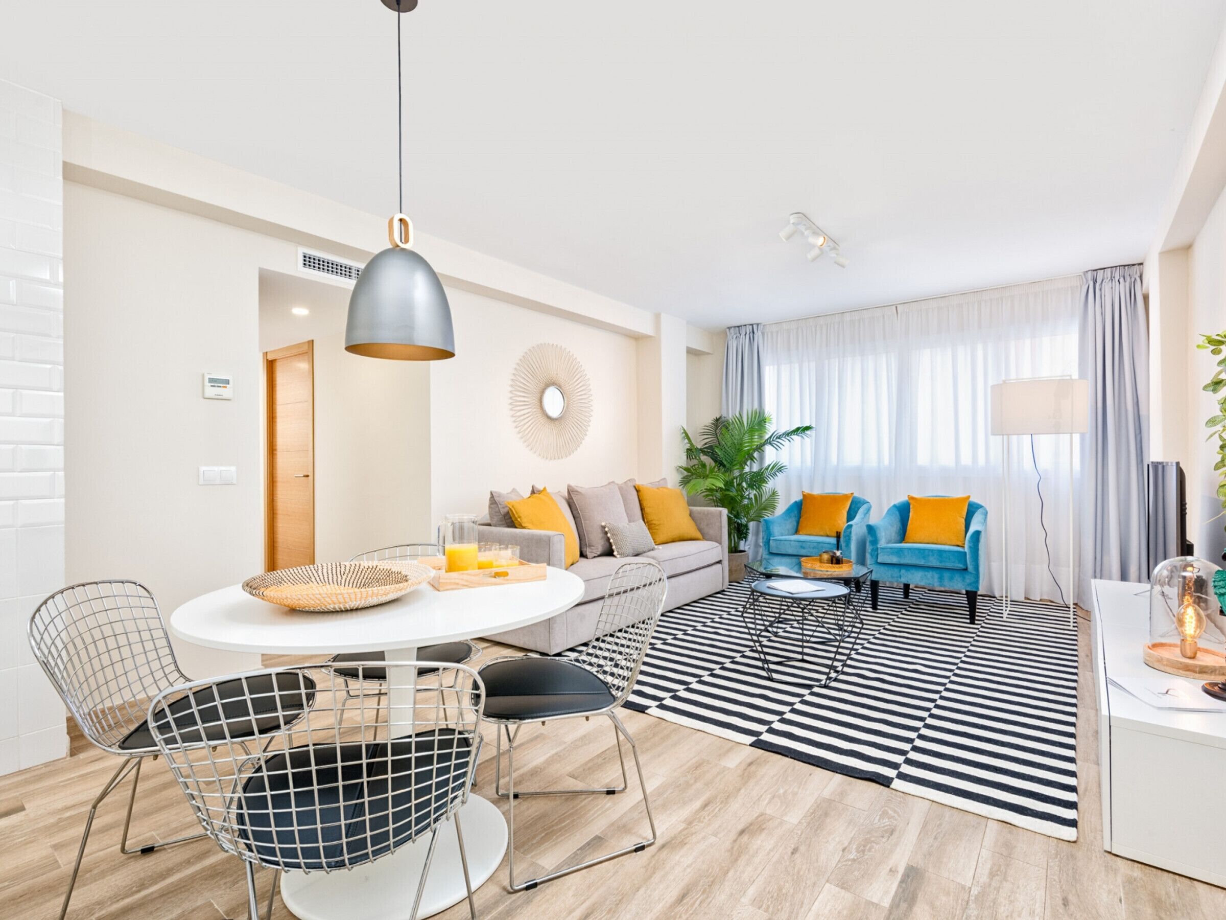 Una sala de estar moderna con un sofá, dos sillones, una mesa de comedor con sillas y un ventanal con cortinas.