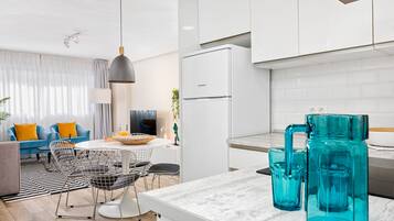 Una cocina moderna con armarios blancos, un refrigerador negro y un comedor con mesa y sillas blancas.