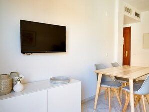 Ein moderner Essbereich mit einem Holztisch und Stühlen, einem Wand-Fernseher und einer weißen Kommode mit Dekoration.