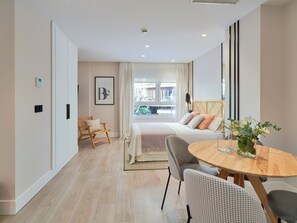 A modern hotel room with a bed, a round wooden table, and a chair. There is a window with a view of buildings outside. - Cozy Studio Near La Malagueta Beach with Air Conditioning and WiFi (Málaga)