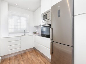Eine moderne Küche mit weißen Schränken, einem Edelstahl-Kühlschrank, einer Mikrowelle und einem Backofen.
