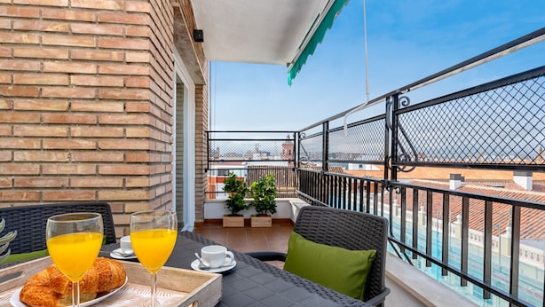 A balcony with a table set for breakfast, including croissants and orange juice, overlooking a cityscape. - Elegant 3-Bedroom Apartment in Malaga City Center with Terrace (Málaga)
