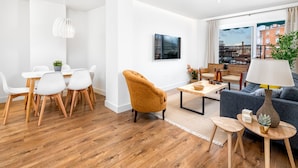 A modern living room with a dining area, a sofa, a coffee table, and a TV mounted on the wall. - Elegant 3-Bedroom Apartment in Malaga City Center with Terrace (Málaga)