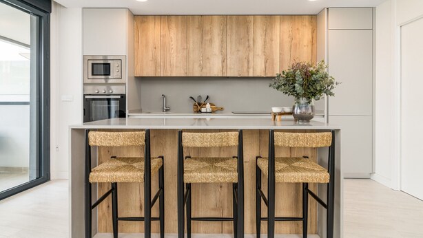 Una cocina moderna con armarios de madera, una isla central con taburetes de bar, un microondas y un florero con flores.