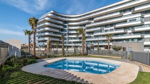 Un hotel moderno de varios pisos con piscina rodeada de palmeras y césped cuidado.