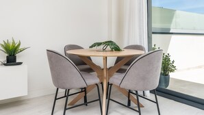 Un comedor moderno con una mesa redonda de madera, cuatro sillas grises tapizadas y una lámpara colgante.
