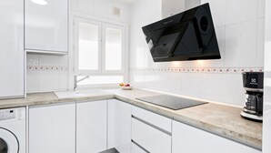 Eine moderne Küche mit weißen Schränken, einer integrierten Waschmaschine, einem flachbildfernseher über der Arbeitsfläche und einer Kaffeemaschine auf der Arbeitsplatte.